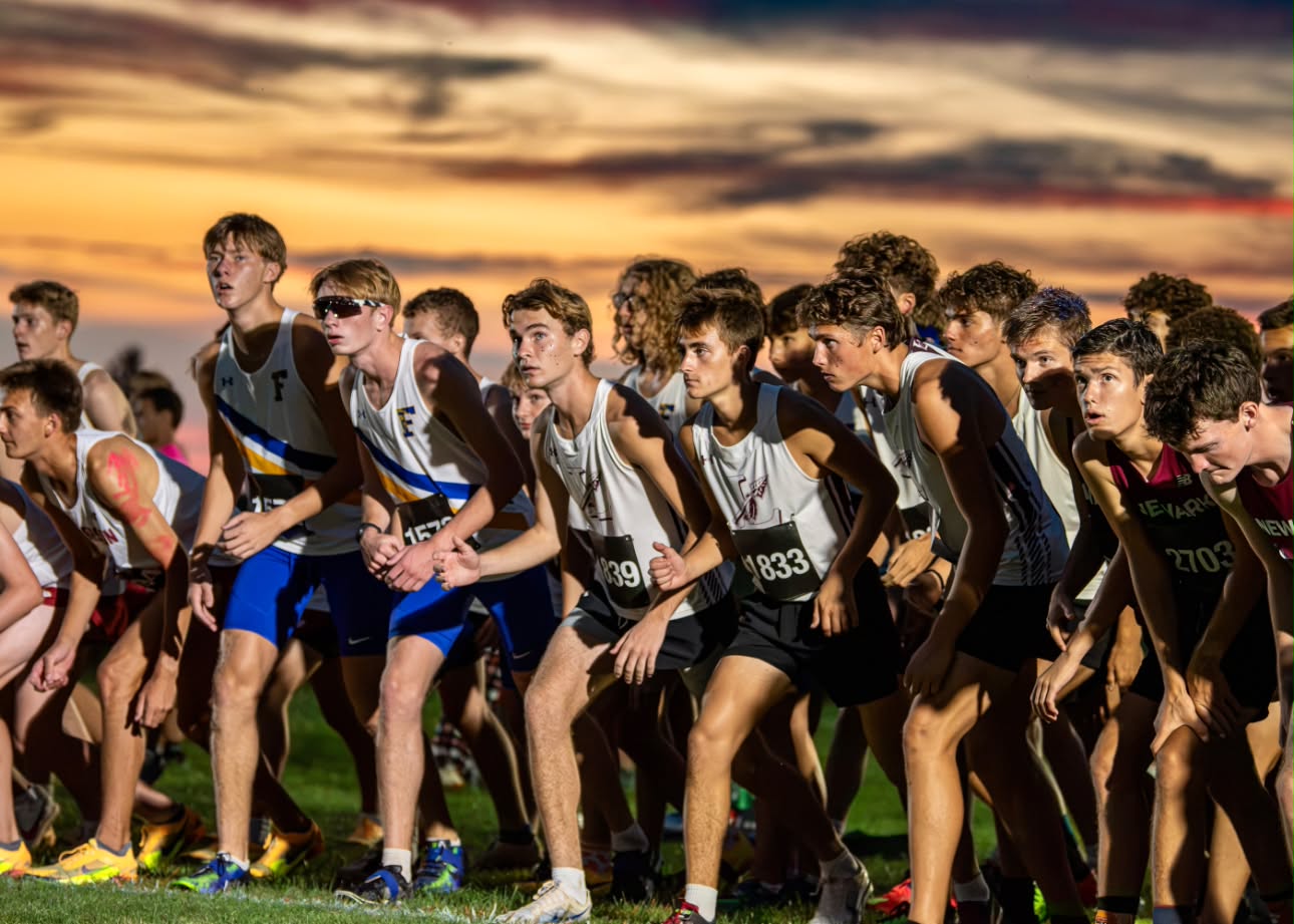 Boys cross country runners lined up at the starting line under a sunset sky